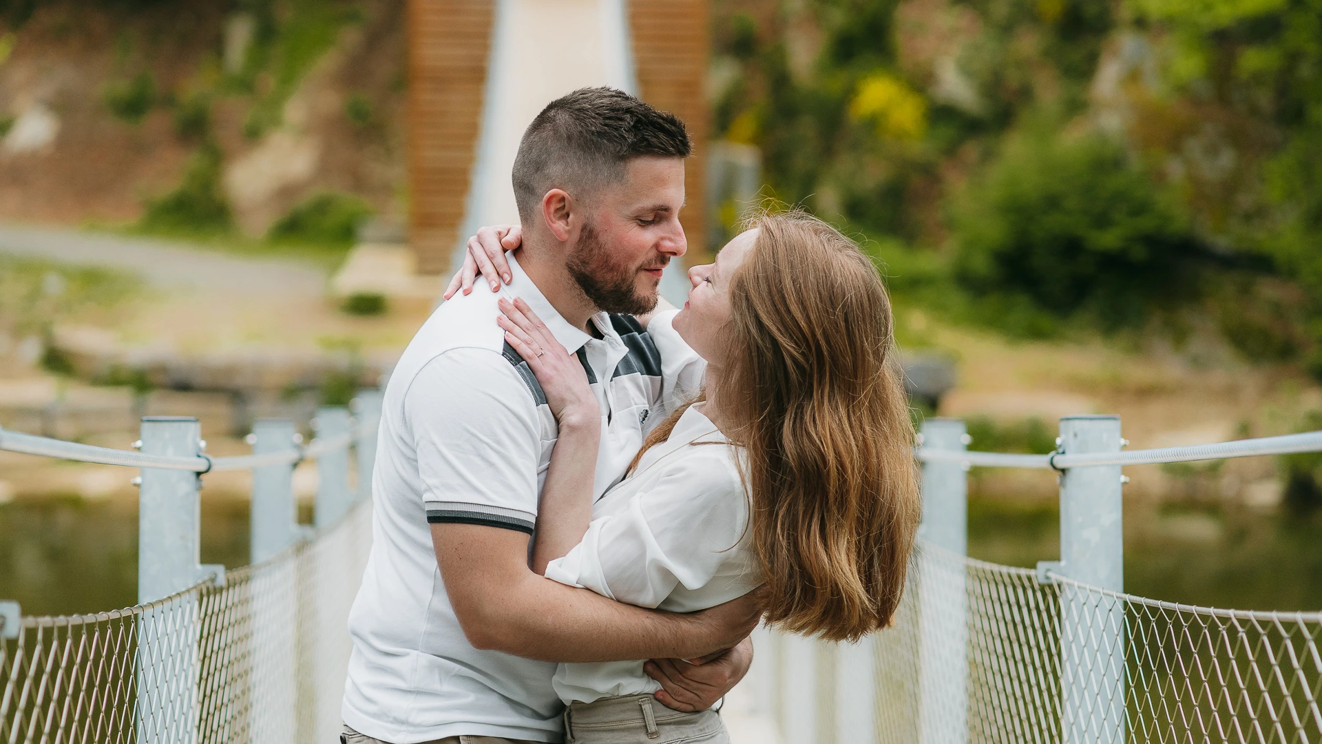 Un couple s'embrassant sur un pont au-dessus d'une rivière.