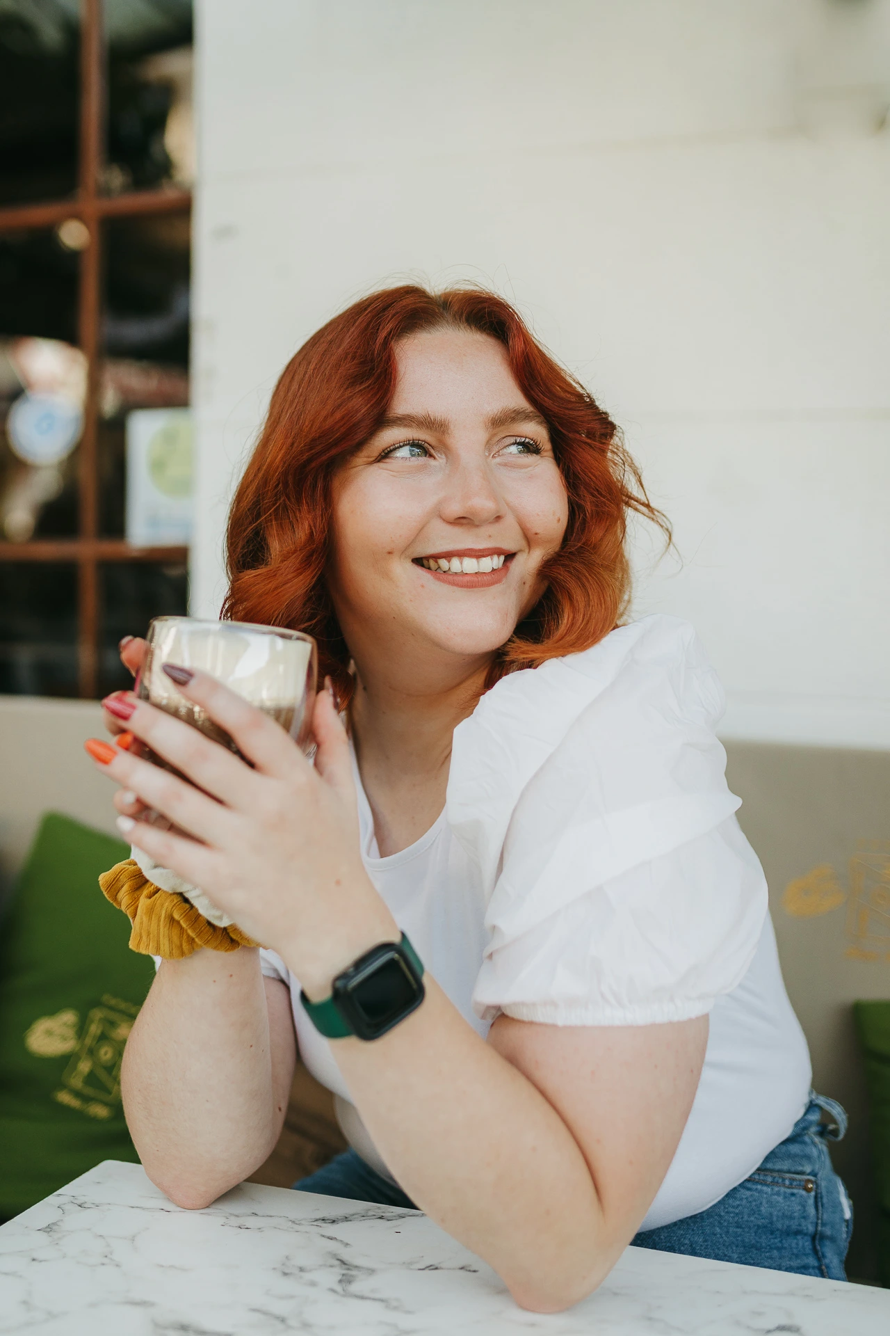 Femme souriante et tenant un verre à une table de café.