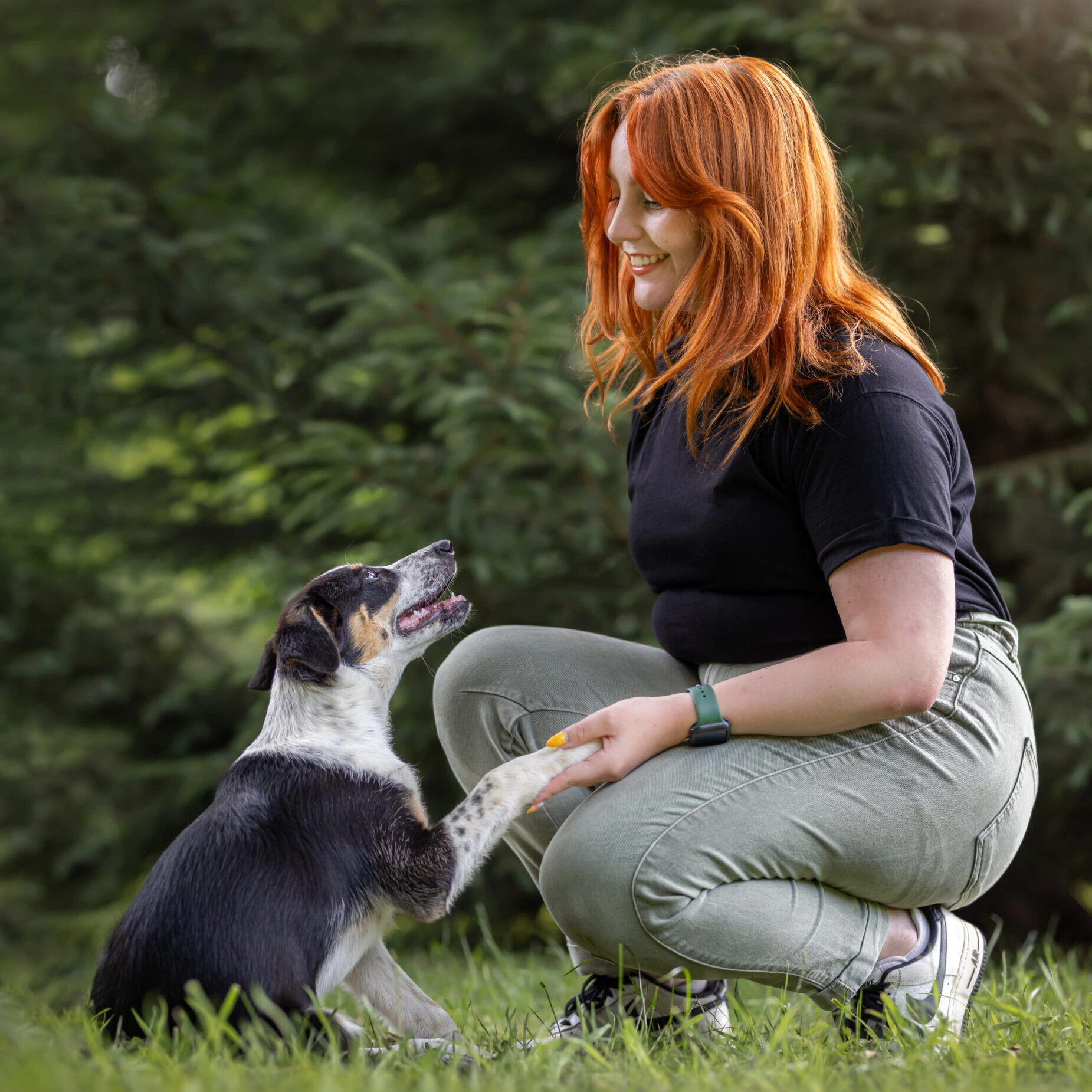 Une femme agenouillée avec son chien dans l'herbe.